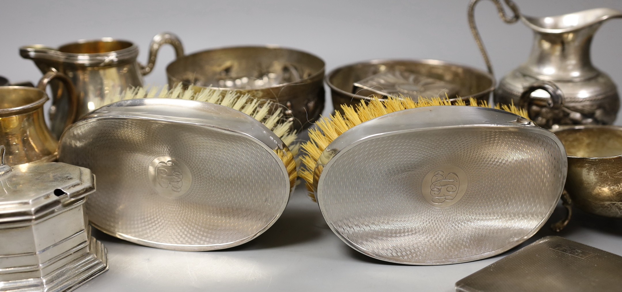Mixed silver and white metal items including par of toastracks, sugar bowl match sleeve, sauceboat, cream jug, Victorian christening mug, pair of silver mounted clothes brushes, silver mustard silver cigarette case, 25.8